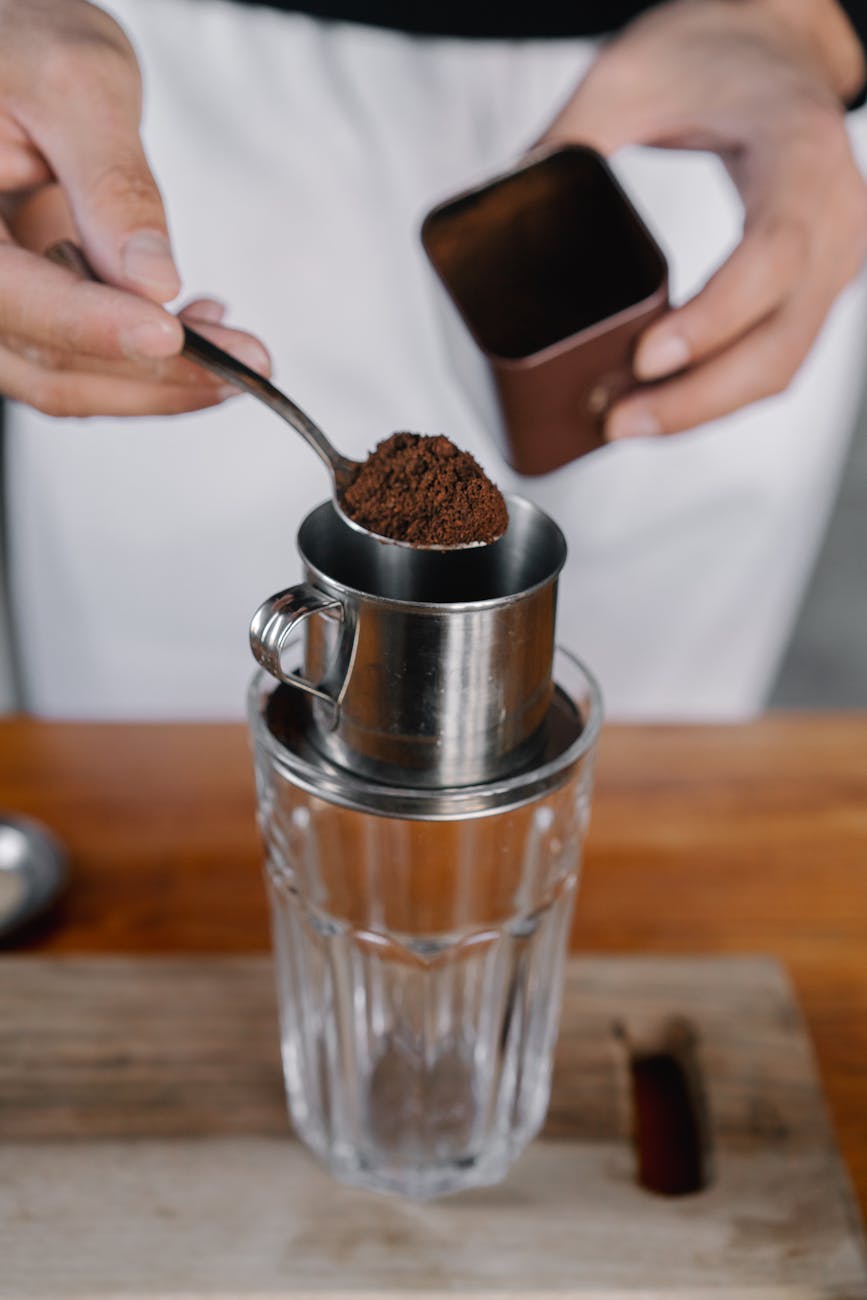 Close-up of coffee preparation using metal filter and glass cup.