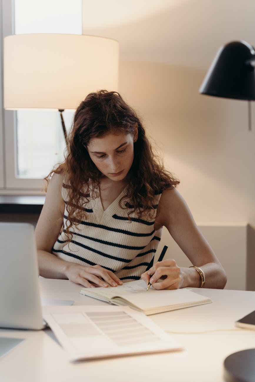 Professional woman focused on writing at a modern office desk, ambient lighting