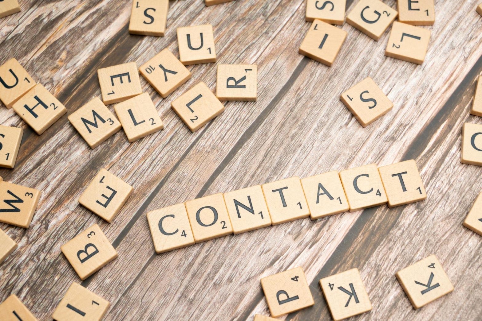 Scrabble-style letter tiles spelling 'contact' on wooden surface.