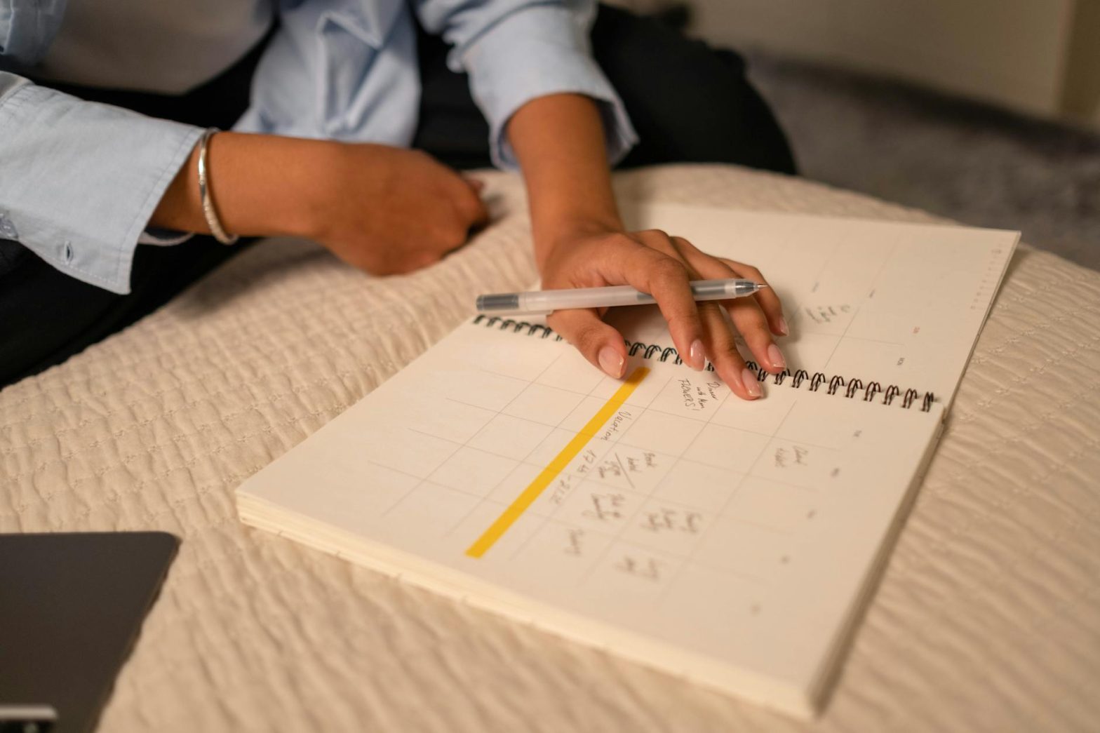 Close-up of a person scheduling in a spiral-bound planner using a pen. Indoor setting.