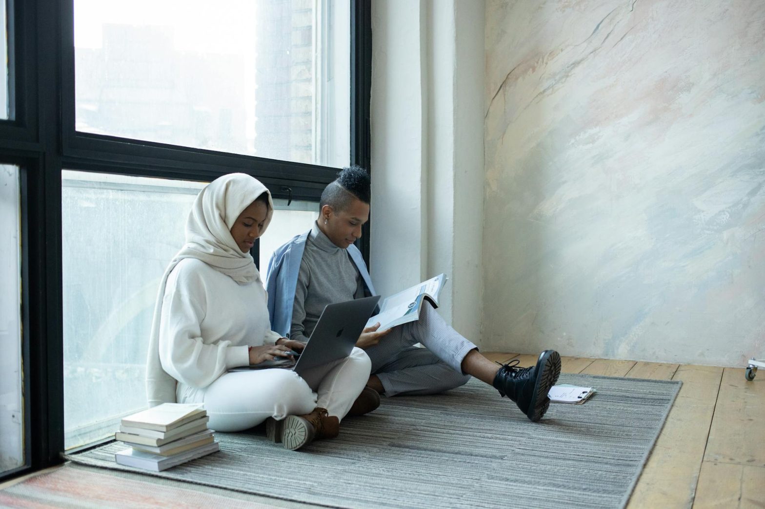 Two students focusing on studies with laptop and books in a peaceful indoor setting.