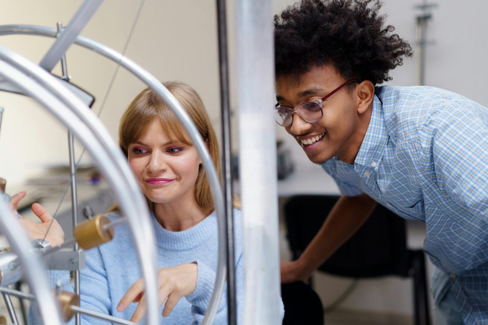 Caucasian woman and African man interacting with physics apparatus in a classroom setting.