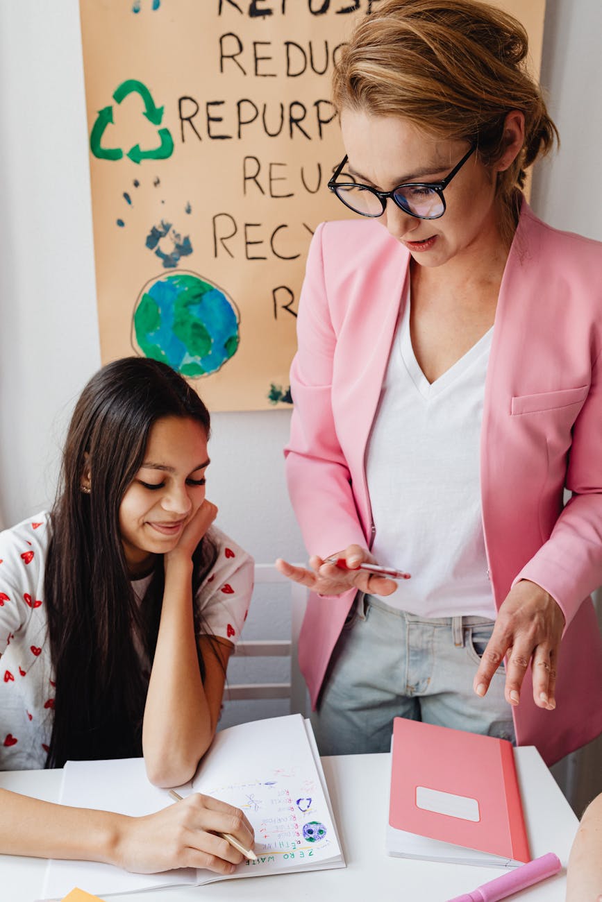 Female teacher assisting teenage girl with homework in classroom setting.