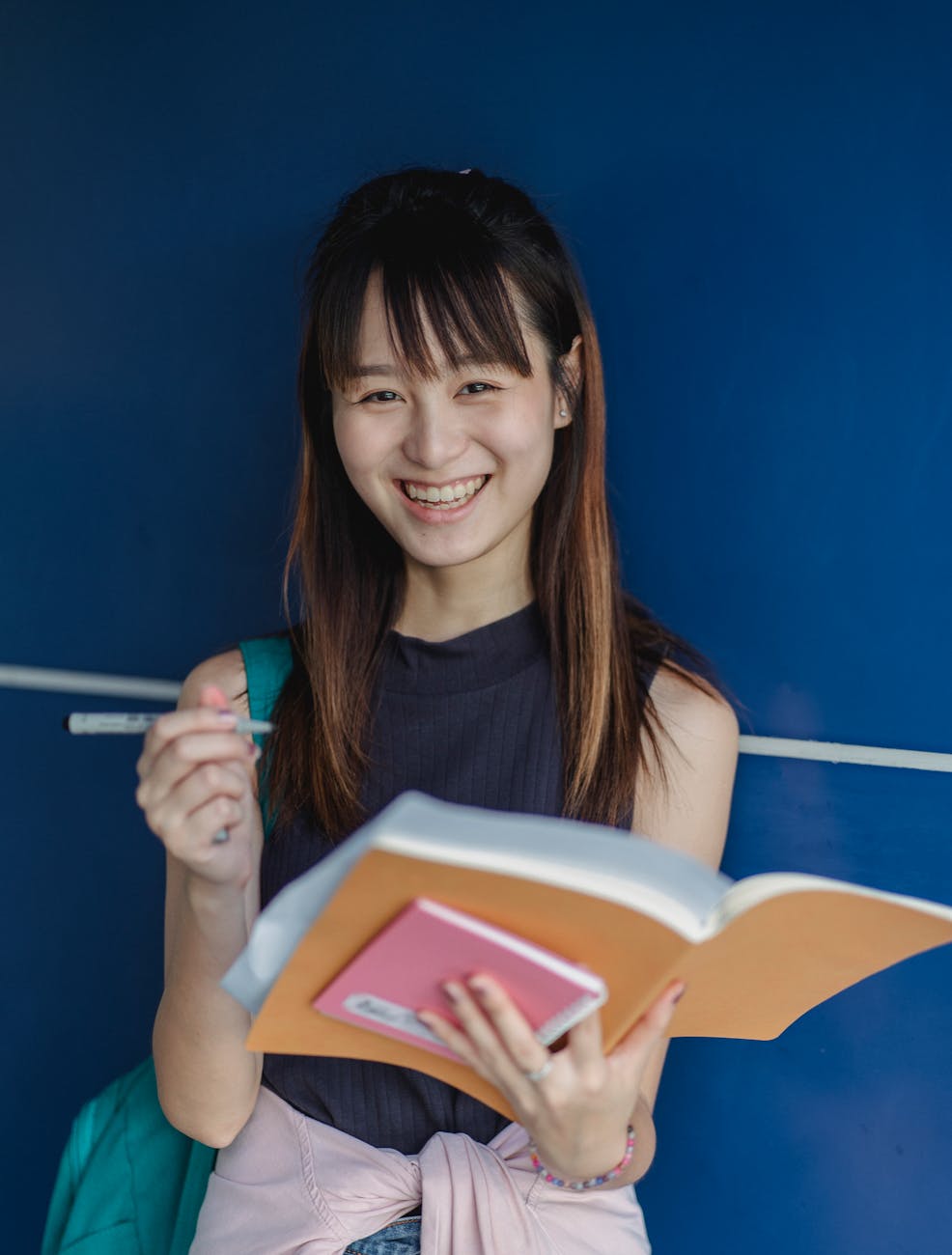 Young Asian woman smiling while studying with books indoors, embodying joy in education.